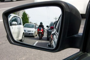A motorcycle is reflected in the side-view mirror of a car. Motorcycle accident victims can call New Haven attorneys for help.