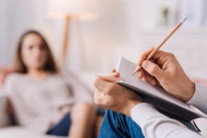 A psychiatrist writes notes on a pad while speaking with their patient. Contact a Connecticut psychiatric malpractice lawyer.