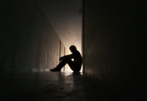 A man sits in a dark hallway before contacting a New Haven clergy abuse lawyer.